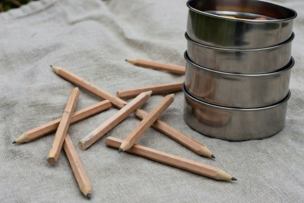 Close-up detail of woven linen picnic fabric, carpenter pencils, and stacked stainless steel fruit containers